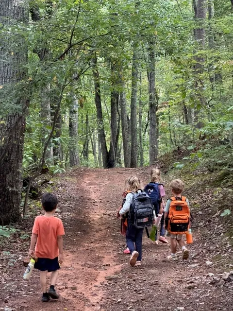 Children hiking up a forest trail with their backpacks
