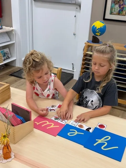 Two girls working with sandpaper letters at a classroom table