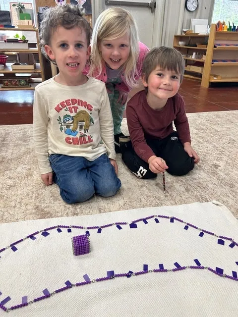 Three children smiling beside a bead chain layout